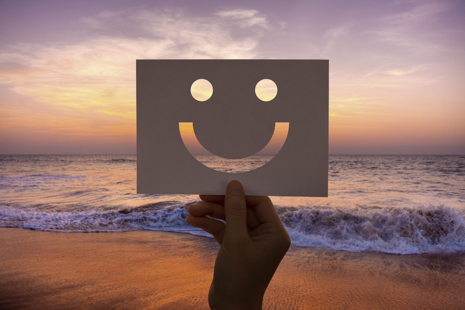 Un smiley montré à la main avec le couché du soleil en fond à la plage.